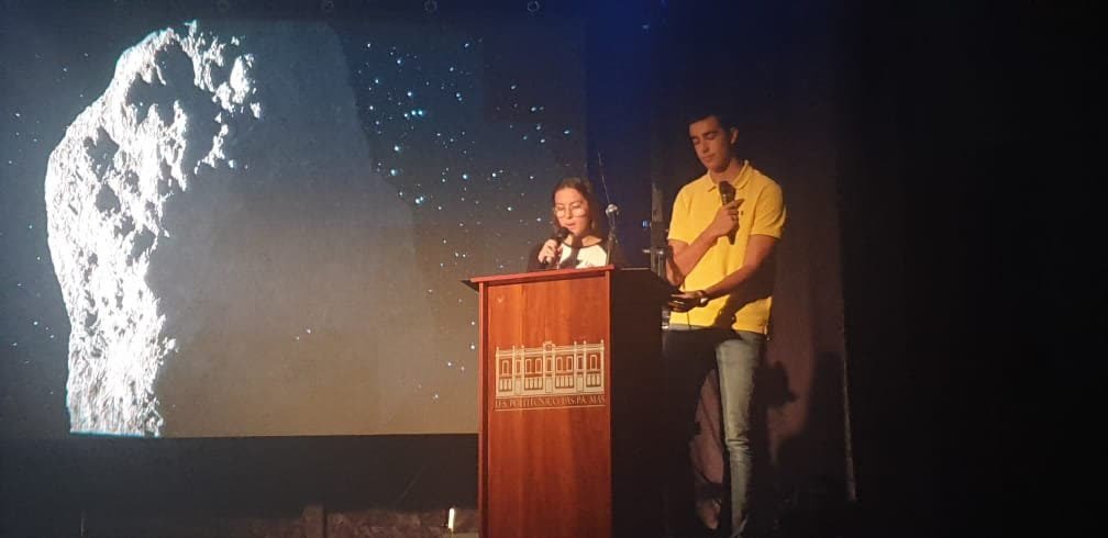 Alumnado presentando el proyecto con un asteroide proyectado en el escenario