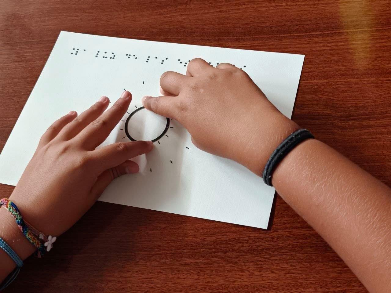 Niño explorando con las manos un diagrama táctil en braille sobre la formación de una estrella