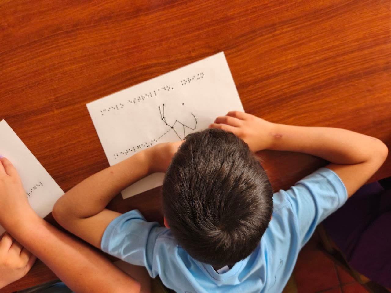 Dos niños comparando láminas táctiles en braille con la constelación de Orión