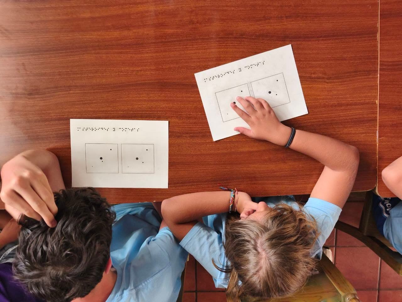 Niños manipulando maquetas táctiles de asteroides junto a láminas en braille sobre caza de asteroides