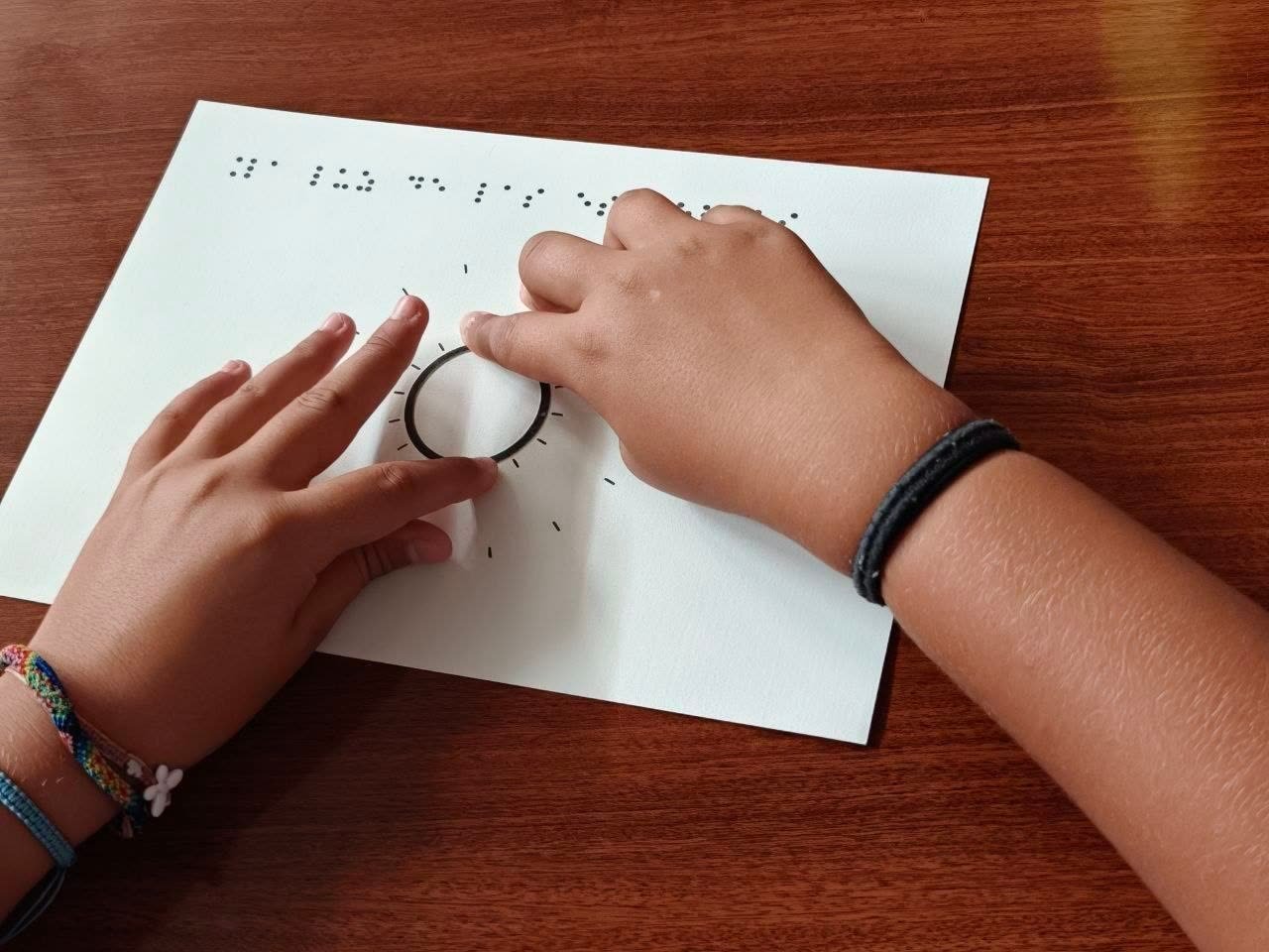 Una persona explora con las manos un diagrama táctil en braille sobre la formación de las estrellas, en un taller de astronomía accesible de la AAEC