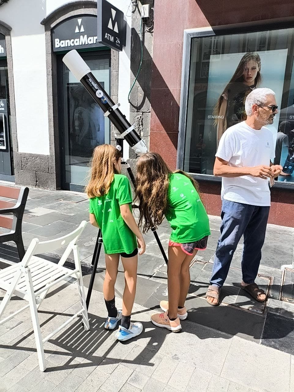 Dos niñas miran el Sol por el telescopio solar junto a un miembro de la AAEC