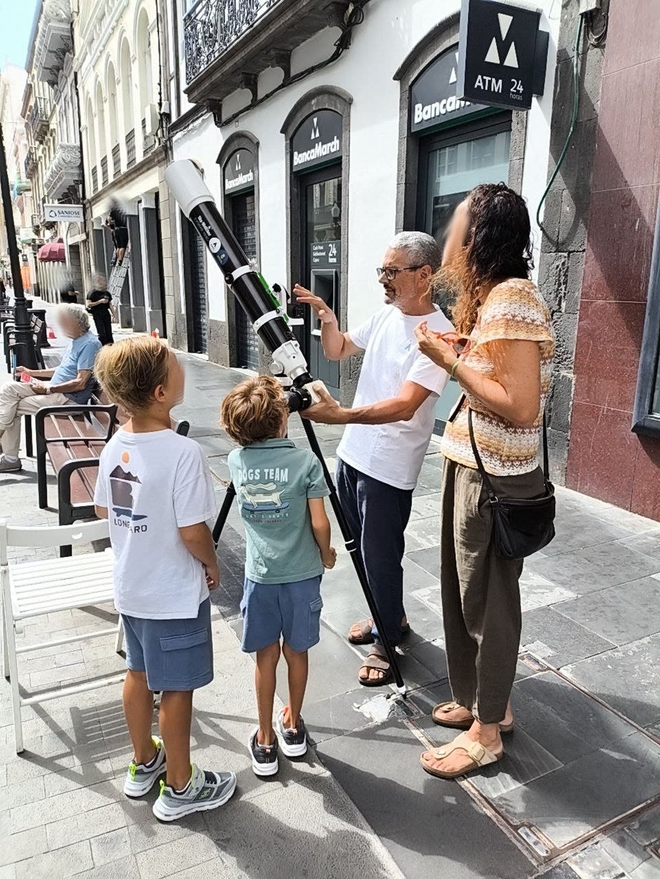 Un miembro de la AAEC ayuda a dos niños a mirar el Sol por el telescopio, acompañados por una mujer