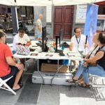 Mesa de talleres con una pareja en la búsqueda de asteroides y una familia conociendo diagramas táctiles